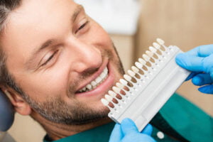 Paciente sonriente comparando tonos de dientes con guía de color en un blanqueamiento dental profesional.