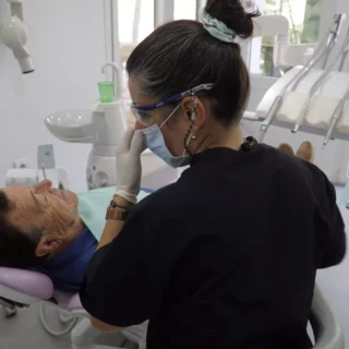 Dentista con atuendo profesional negro revisando a un paciente masculino reclinado en una silla dental en la clínica dental Avilés Digital Dental Clinic, iluminada y moderna.